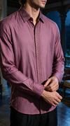 A man wearing a long-sleeve button-up shirt in dusty rose or mauve, featuring decorative embroidered detailing on the collar, placket, and cuffs. The photo is cropped from the chin down, showing his hands adjusting the cuff.