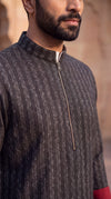 A close-up of a man wearing a dark charcoal gray ribbed knit quarter-zip jacket with a stand collar, set against a warm, blurred background.