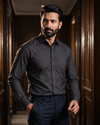 A man wearing a black silk long-sleeve button-down shirt with subtle stingray embroidery on the right sleeve.