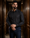 A man wearing a black silk long-sleeve button-down shirt with subtle stingray embroidery on the right sleeve.