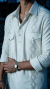 A close-up of a man wearing a white long-sleeve button-up shirt with gray geometric embroidered patterns on the chest and waist, paired with a silver watch.