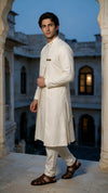 A man modeling a traditional Indian outfit consisting of a cream-colored textured  angarkha kurta and matching trousers