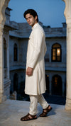 A man modeling a traditional Indian outfit consisting of a cream-colored textured  angarkha kurta and matching trousers