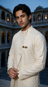 A man modeling a traditional Indian outfit consisting of a cream-colored textured  angarkha kurta and matching trousers