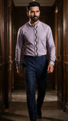 A man wearing a lavender long-sleeve shirt with a decorative black scalloped placket and navy trousers, walking down a dark wood-paneled hallway.