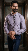 A man wearing a lavender long-sleeve kurta with a distinctive black wavy vertical stripe down the front placket and matching patterned cuff, paired with navy trousers, standing in a dimly lit hallway.