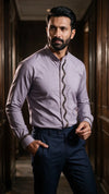 A man wearing a lavender long-sleeve kurta-style shirt with a decorative dark zigzag placket and navy trousers, standing in a dimly lit wooden hallway.