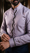 A man wearing a lavender long-sleeve shirt with a dark wavy embroidered or beaded front placket and matching cuff embellishments, shown in a close-up lifestyle shot.