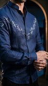 A man wearing a navy blue long-sleeve button-up shirt with white embroidered bird patterns across the chest, shown in a close-up lifestyle shot.